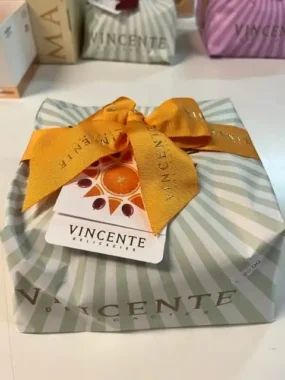 Panettone Vincente da 1000 grammi, confezione in carta con fondo grigio beige e strisce grigio verdi molto delicate ed eleganti. Un fiocco arancione soft a chiusura.